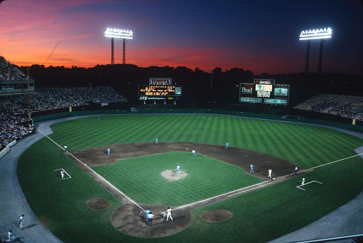 Nighttime view of a baseball game under bright lights with a colorful sunset