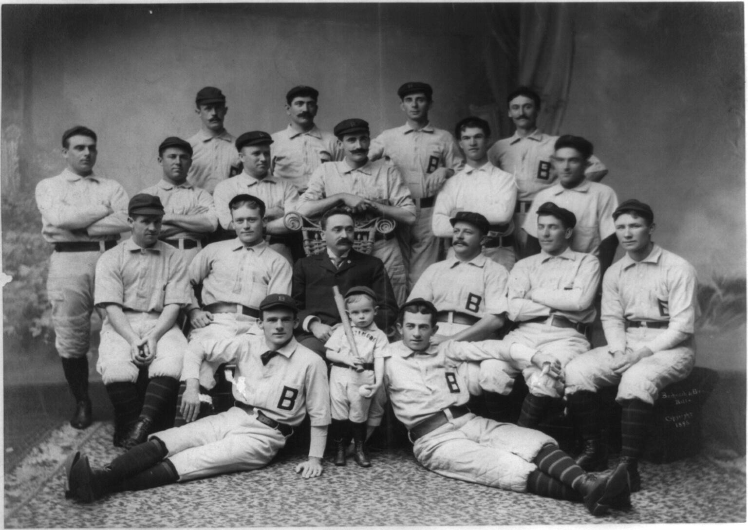 Early Baltimore Orioles team posed in studio with a small batboy in front.