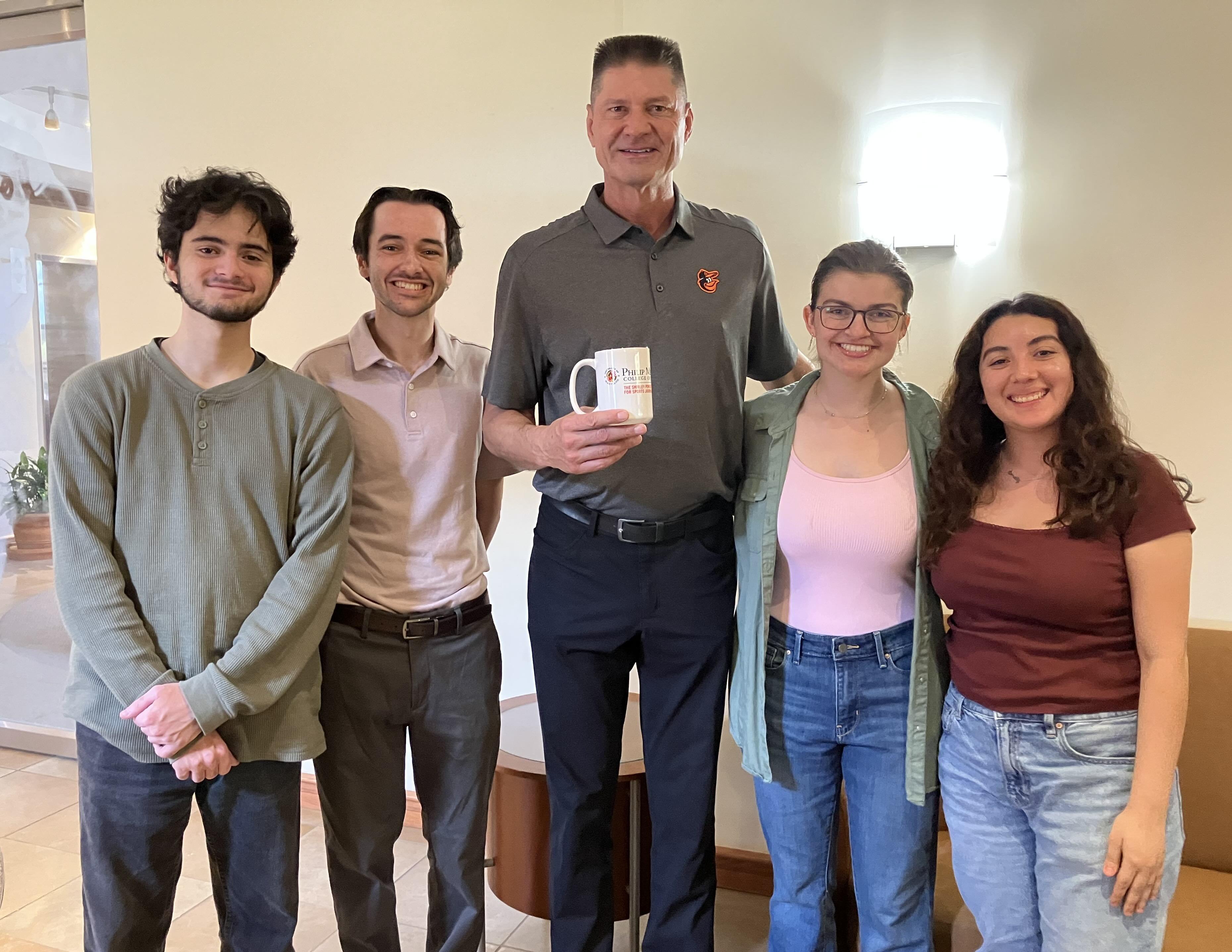 Man standing with four young adults smiling for a photo indoors.