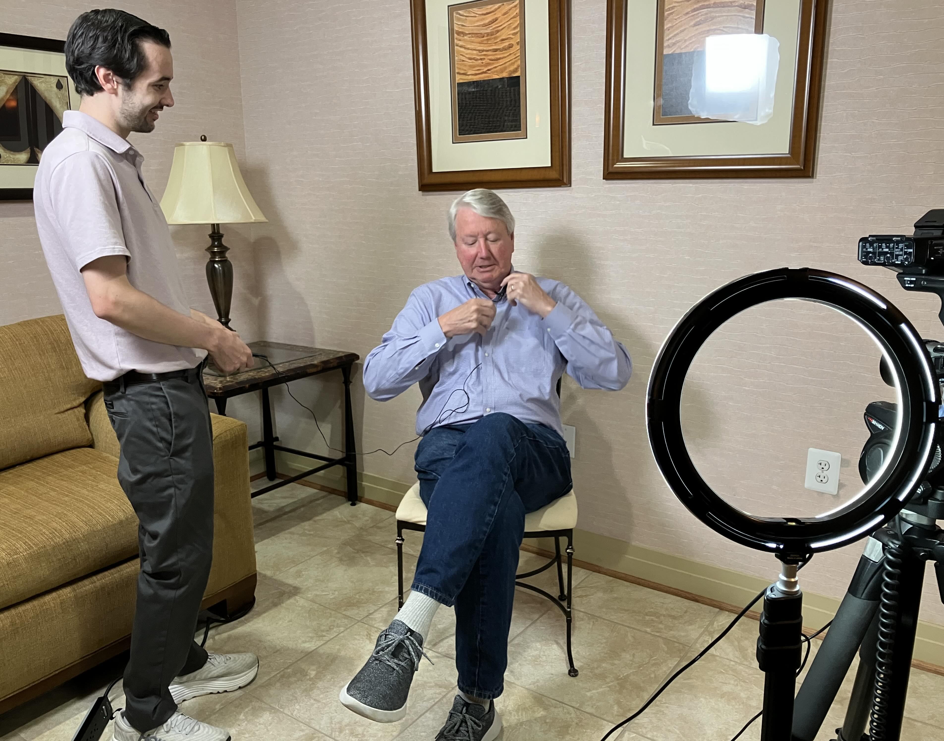 Man adjusting a microphone while a crew member prepares filming equipment and lighting.