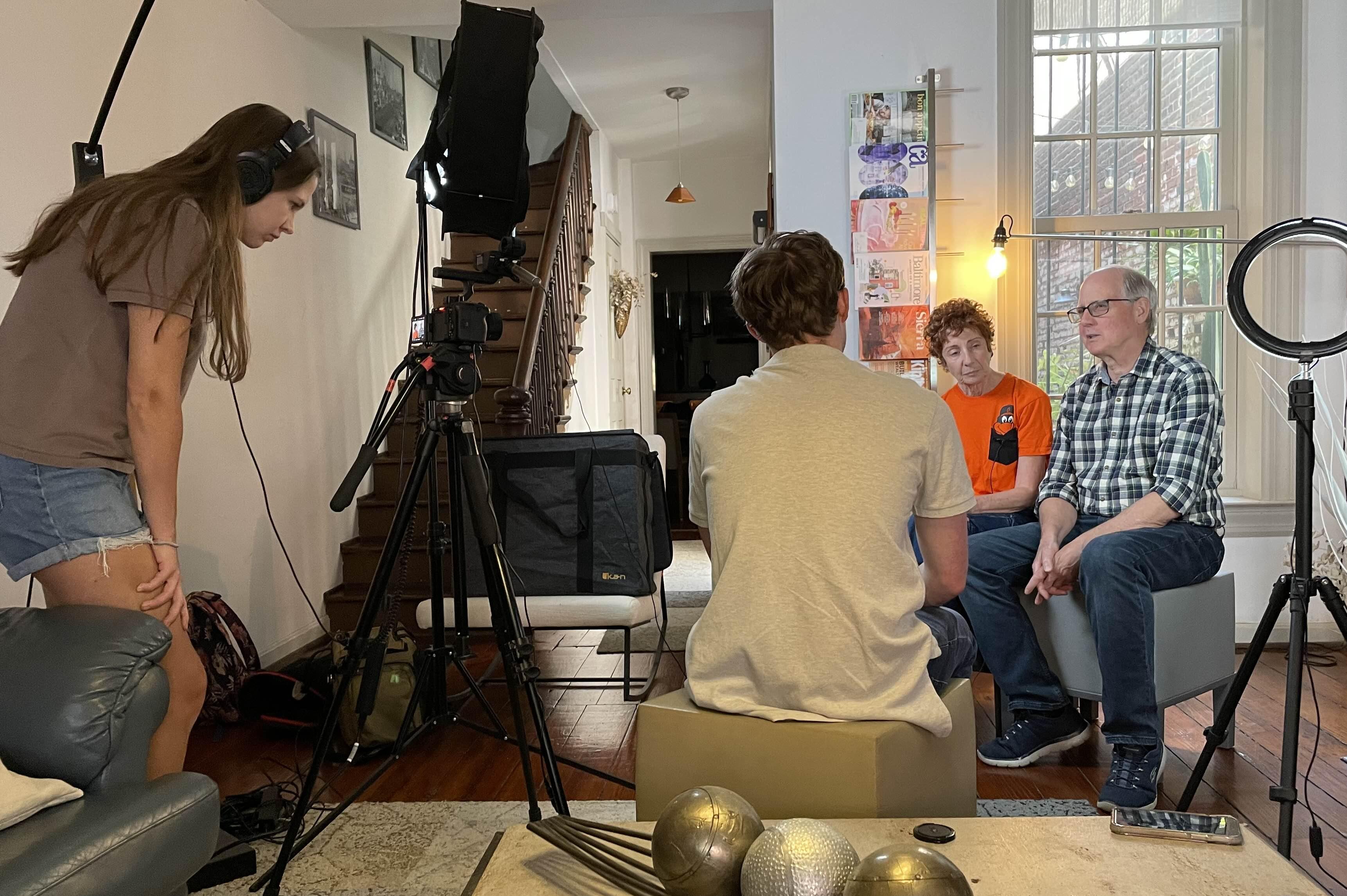Two people being interviewed in a living room while a small film crew records the conversation.