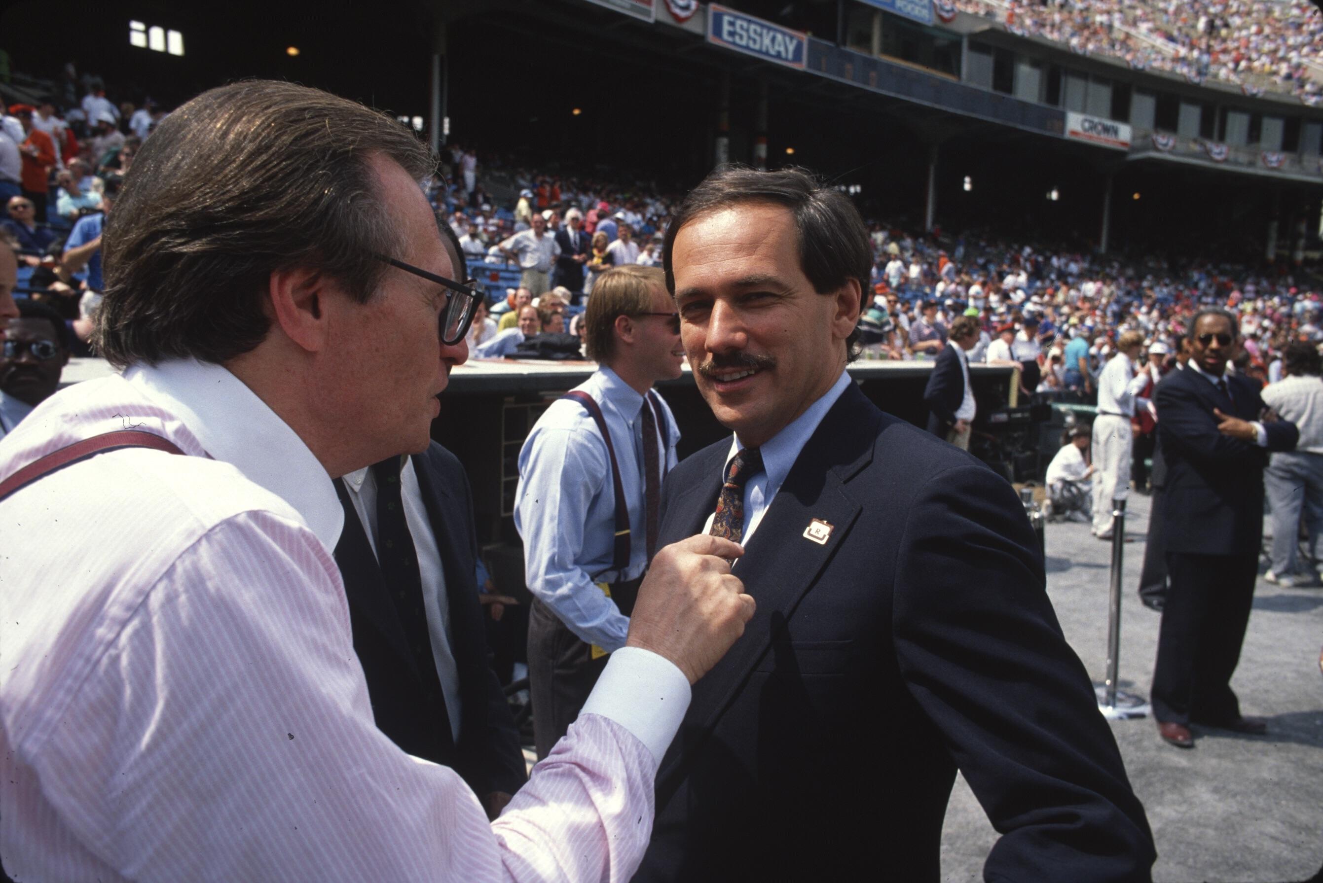 Two men talk on the field at a packed baseball stadium before a game.