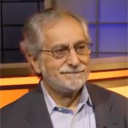 Man with gray hair and glasses smiles during a studio interview.
