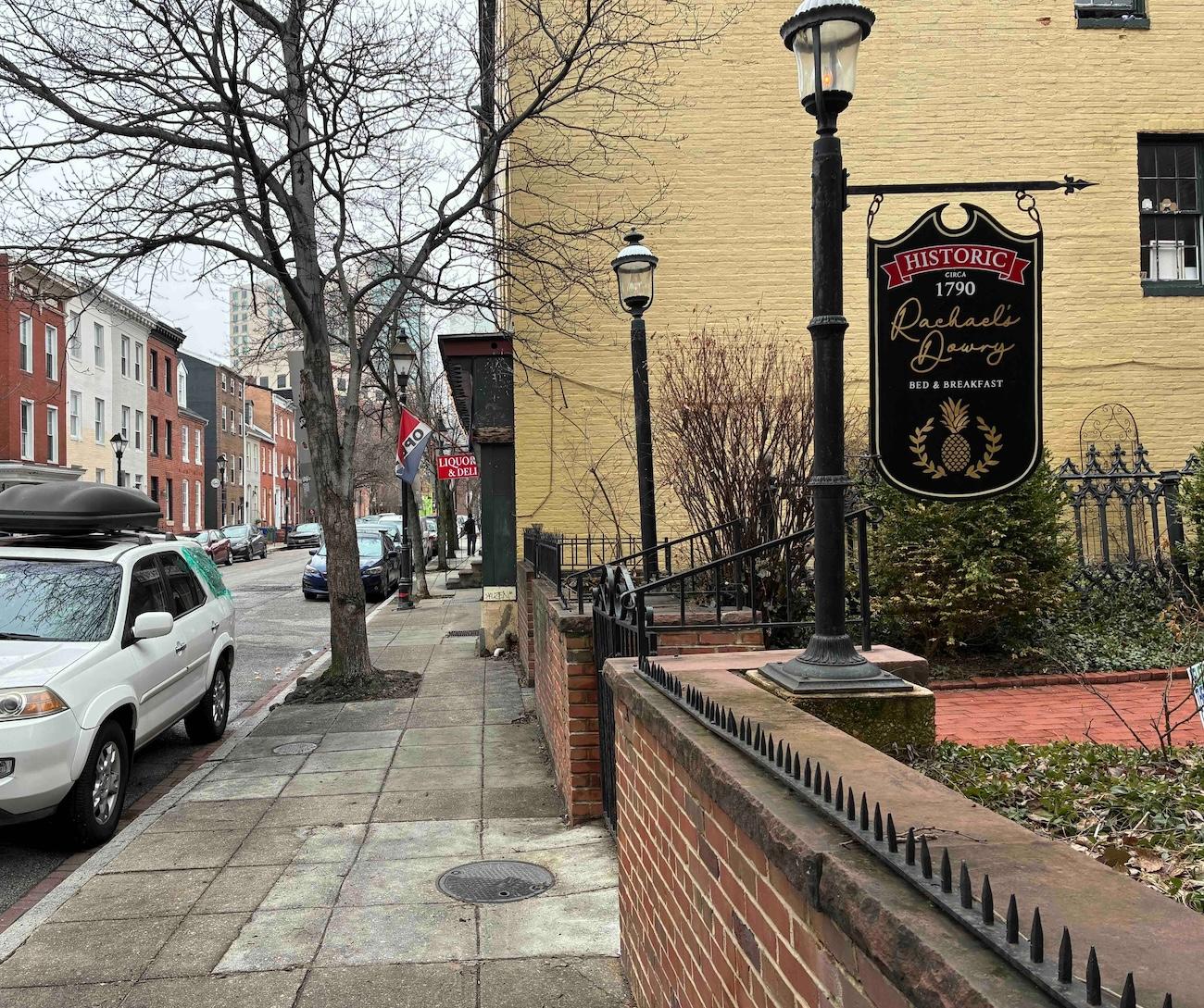 Baltimore street and sidewalk with a red and black neighborhood sign that says "Ridgely's Delight"