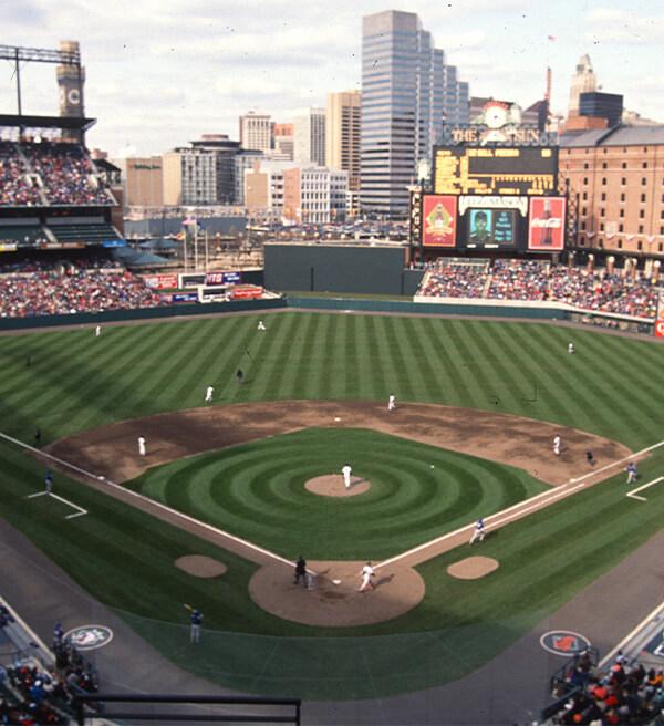 Wide view of a baseball game in progress at Oriole Park at Camden Yards with the scoreboard and Baltimore skyline in the background.